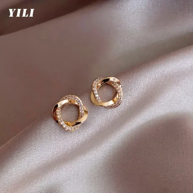 Elegant twisted gold stud earrings with sparkling crystals on soft satin fabric, exuding unique charm
