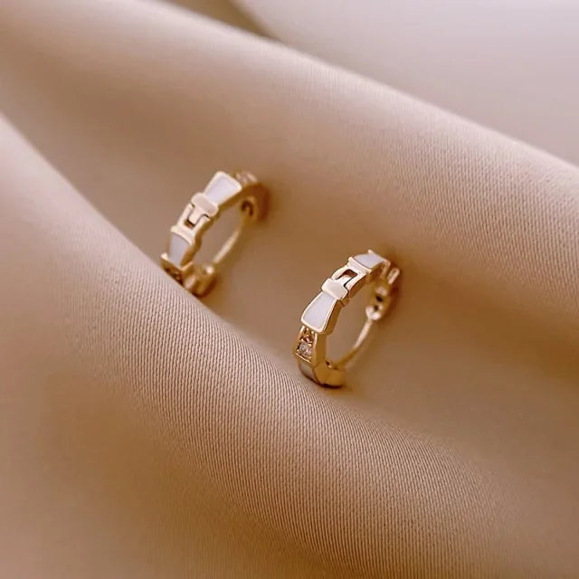 Elegant gold hoop earrings with unique geometric accents on soft beige fabric, inspiring curiosity.