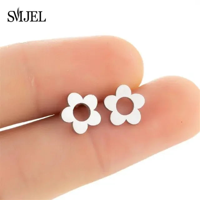 Minimalist silver flower stud earrings held between fingers, playful and modern jewelry