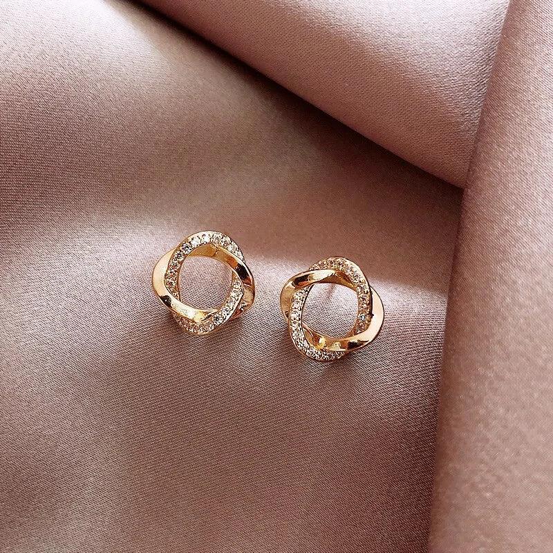 Gold twisted knot earrings with sparkling crystals on elegant satin fabric, inviting curiosity.