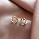 Gold twisted knot earrings with sparkling crystals on elegant satin fabric, inviting curiosity.