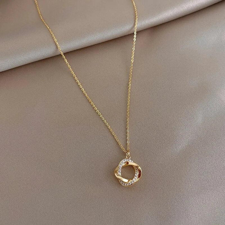 Elegant gold necklace with a sparkling twisted circle pendant on a soft beige background