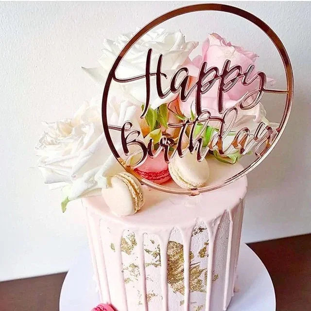Elegant pink birthday cake with gold accents, fresh roses, macarons, and a unique Happy Birthday topper.