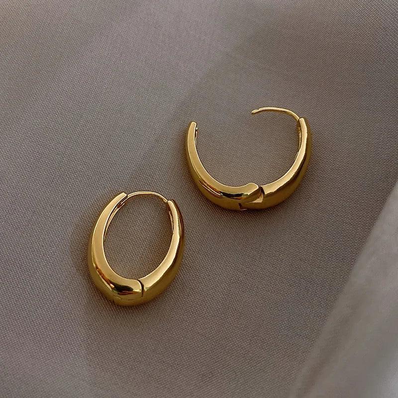Elegant gold hoop earrings with a unique sculptural design on soft fabric, perfect for standout style
