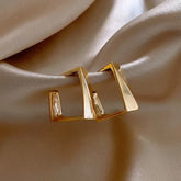 Modern geometric gold earrings with unique angular design on elegant satin background