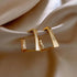 Modern geometric gold earrings with unique angular design on elegant satin background