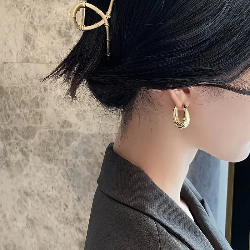 Elegant woman wearing bold gold hoop earrings and a unique gold hair clip, sparking curiosity