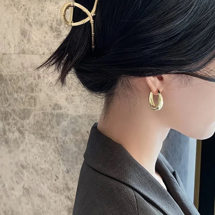 Elegant woman wearing bold gold hoop earrings and a unique gold hair clip, sparking curiosity