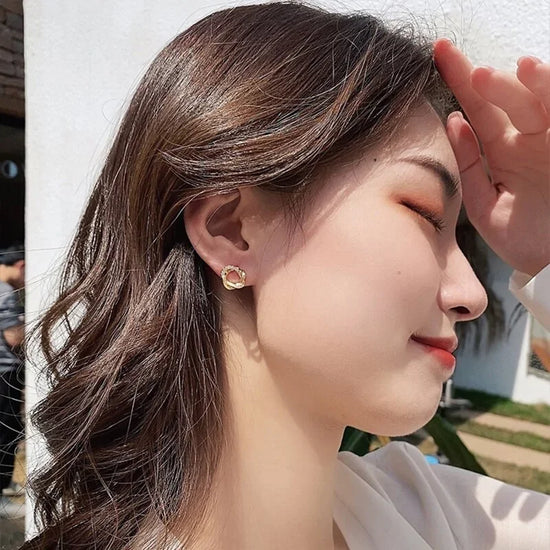 Woman wearing unique gold stud earrings, beautifully catching sunlight, sparking curiosity