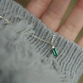 Elegant gold necklace with green gemstone pendant, eye-catching jewelry against cozy grey knit