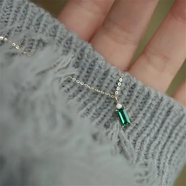 Elegant gold necklace with green gemstone pendant, eye-catching jewelry against cozy grey knit