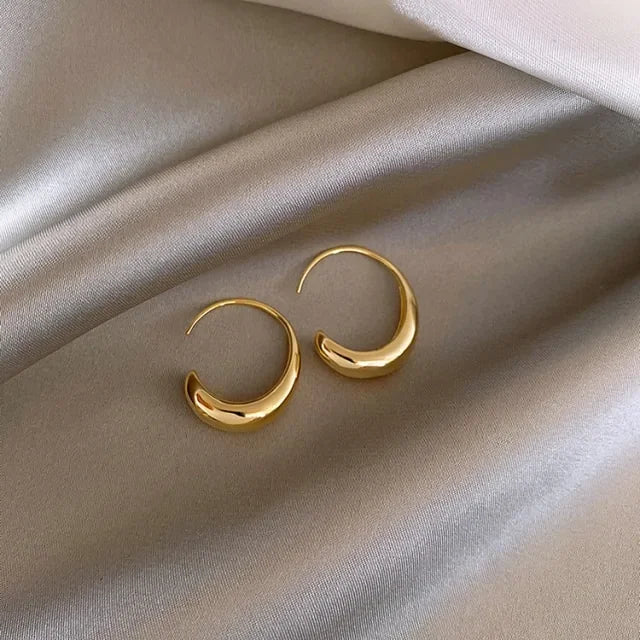 Curved gold hoop earrings on luxurious satin fabric, radiating modern, elegant style.