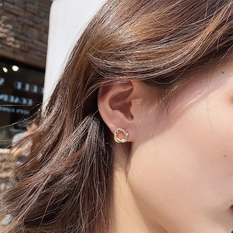 Elegant gold twisted circle stud earring, sparkling and unique, shown on a woman&