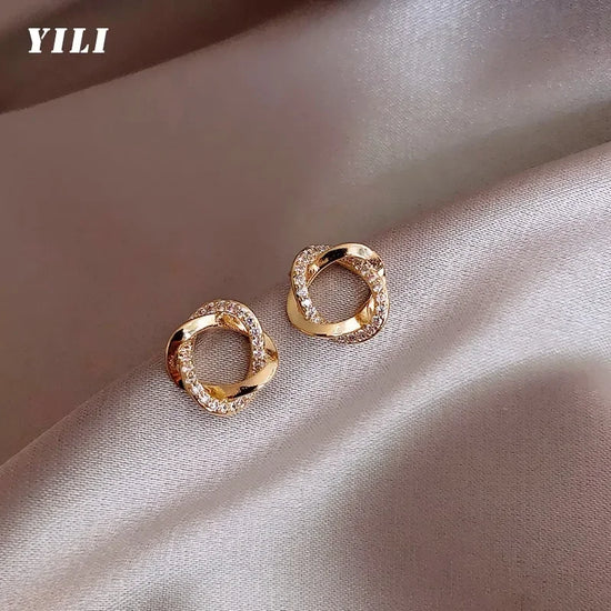 Dazzling gold twisted hoop stud earrings sparkle on elegant satin, perfect for unique style