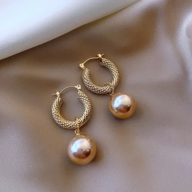 Elegant gold hoop earrings with textured design and unique pearl drops on satin fabric