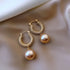 Elegant gold hoop earrings with textured design and unique pearl drops on satin fabric