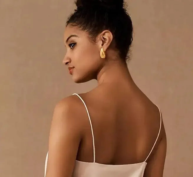 Elegant woman in gold teardrop earrings and chic white dress, capturing unique jewelry style