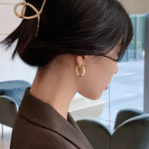 Elegant woman with gold hoop earrings and unique hair clip, exuding modern, stylish charm