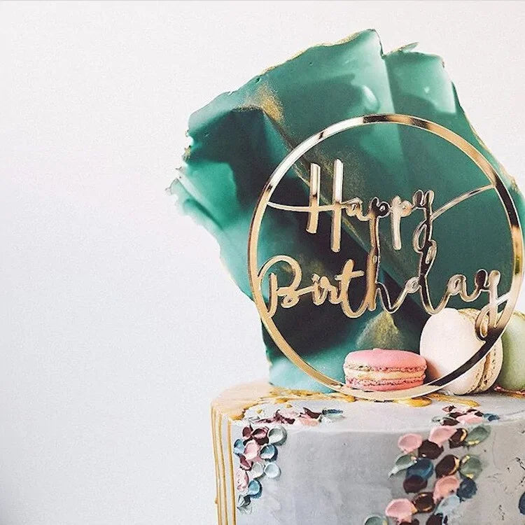 Elegant birthday cake with gold acrylic topper, teal sugar accent, and colorful macarons