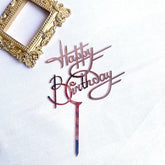 Elegant rose gold Happy Birthday cake topper beside ornate gold picture frame, perfect for unique celebrations.