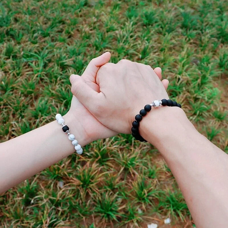 Couple holding hands outdoors, wearing unique black and white beaded bracelets, symbolizing connection.