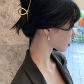 Elegant woman wears unique gold hoop earrings and bamboo hairpin, inspiring chic curiosity.