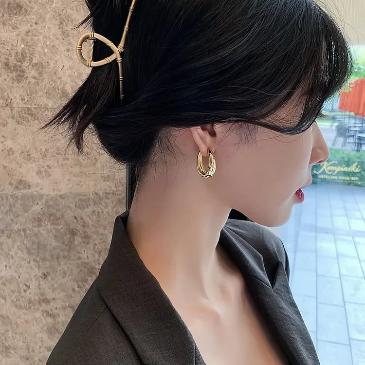 Elegant woman wears unique gold hoop earrings and bamboo hairpin, inspiring chic curiosity.