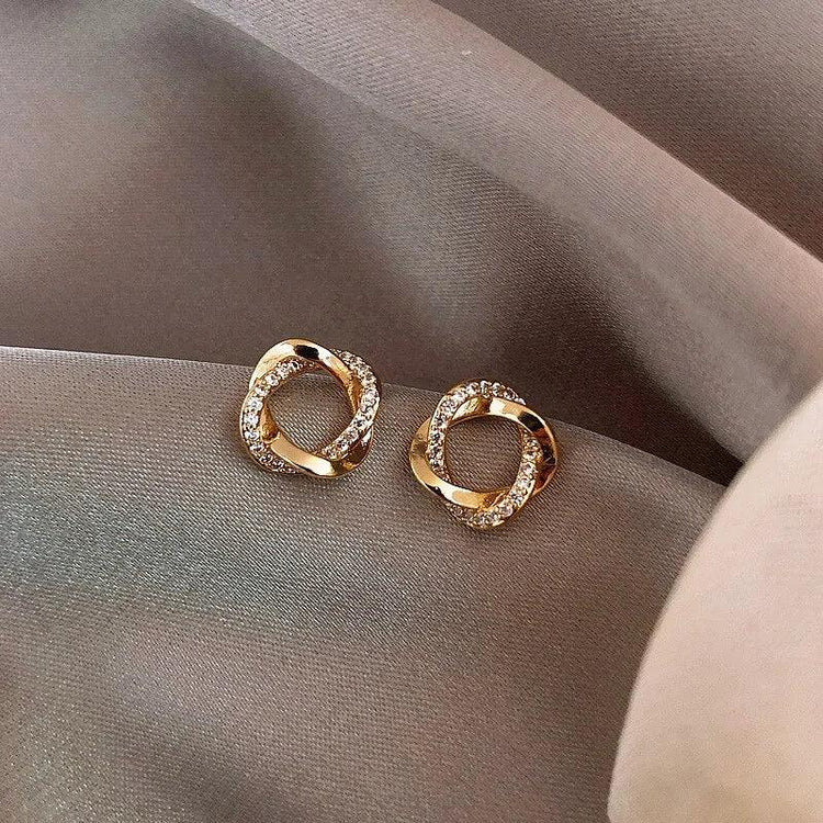Dazzling gold knot stud earrings with sparkling crystals on elegant mauve fabric, unique jewelry