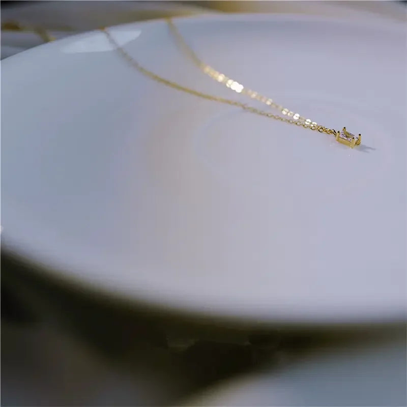 Delicate gold chain necklace with unique rectangular pendant, showcased on a smooth white plate.