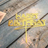 Elegant gold Happy Birthday cake topper on rustic blue wooden surface, perfect for unique celebrations