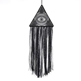Intriguing black triangle macrame wall hanging with eye motif and flowing textured fringe, perfect for unique home décor.