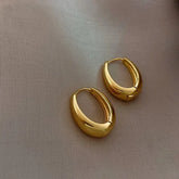 Sleek gold hoop earrings on soft beige fabric, radiating modern minimalist luxury.