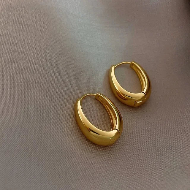 Sleek gold hoop earrings on soft beige fabric, radiating modern minimalist luxury.