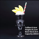 Unique black ceramic face-shaped mug with crushed ice, orange slices, and a striped straw, perfect for stylish décor or creative cocktails.